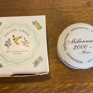 May include: A white porcelain trinket box with a gold rim and the text "Millennium 2000 - Years" in black lettering. The box is decorated with a floral pattern and the words "Falcon China" in a circle.