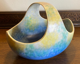 May include: A blue, green, and yellow ceramic bowl with a handle. The bowl has a mottled glaze and a unique shape.