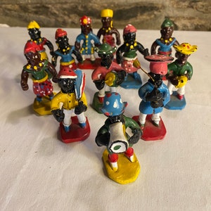 May include: A collection of 12 hand-painted figurines depicting a band of musicians. The figurines are made of a dark brown material and are painted in bright colors, including red, yellow, blue, green, and white. Each figurine is wearing a different outfit and holding a different musical instrument.
