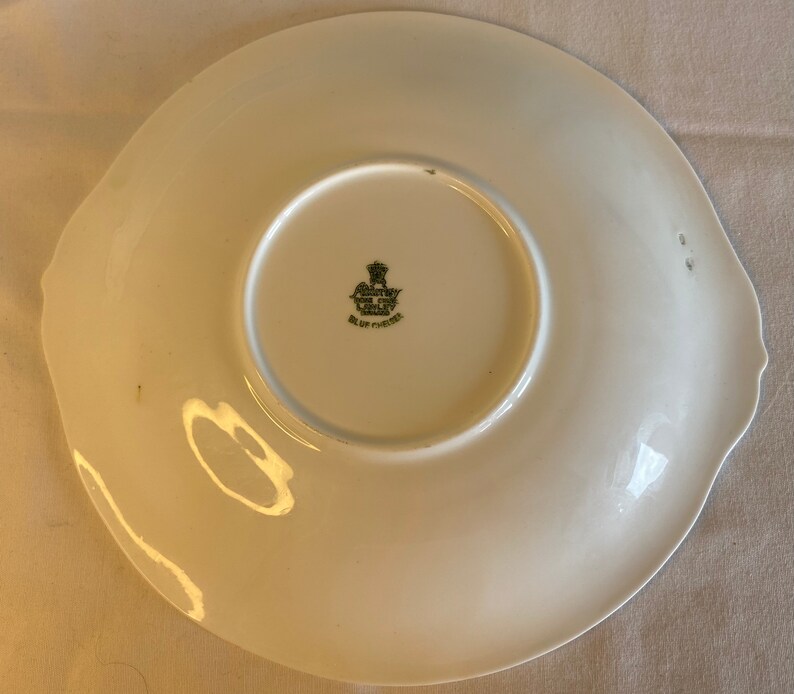May include: White ceramic plate with a scalloped edge and a green and black logo that reads "Country Life Blue of Chelsea" in the center.