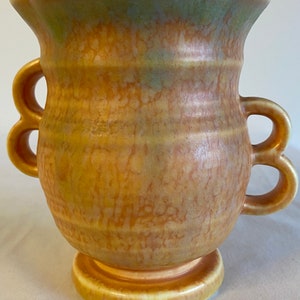 May include: A yellow and orange ceramic vase with a mottled glaze and two handles. The vase has a wide mouth and a round base.