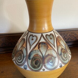 May include: A ceramic vase with a brown, white, and green geometric pattern. The vase has a wide base and a narrow neck.