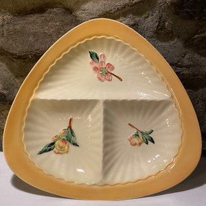 May include: A triangular ceramic serving dish with three sections. The dish has a scalloped edge and a pale yellow rim. Each section features a floral design in shades of pink, green, and yellow.
