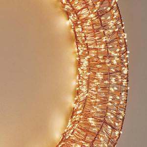 May include: A circular decorative light fixture with warm white LED lights. The lights are woven into a copper-colored wire frame, creating a glowing, festive accent. Ideal for holiday or event decor.
