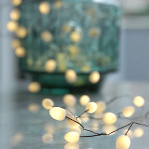 May include: A string of white fairy lights with a warm glow, draped over a textured teal vase. The lights are arranged in a random pattern, creating a whimsical and festive atmosphere.