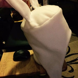 Op de afbeelding: Witte fleece-hoed met twee lange konijnenoren. De hoed is kegelvormig en heeft een puntige punt.