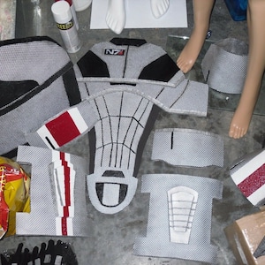 May include: A set of grey and black fabric pieces with red accents. The pieces are labeled with the letters "NZ" and appear to be parts of a costume.