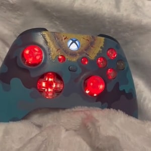 Könnte beinhalten: Ein blauer und grüner Tarn-Xbox-Controller mit roten Knöpfen und einem leuchtend grünen Xbox-Logo.