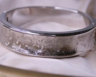 May include: A silver bangle bracelet with a textured, wave-like design.