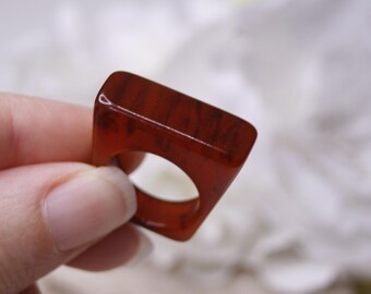 May include: A red square-shaped ring made of resin with a smooth, glossy finish.