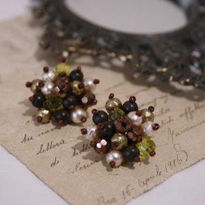 Puede incluir: Un par de pendientes hechos con cuentas marrones, verdes y blancas. Las cuentas están dispuestas en forma de racimo y están unidas a un poste plateado.