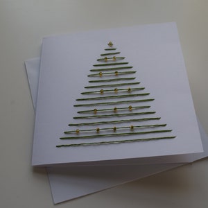 May include: A white card with a green thread Christmas tree design. The tree is decorated with gold beads.