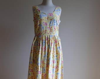 May include: A yellow sleeveless maxi dress with a floral print in shades of pink, blue, and yellow. The dress has a fitted bodice and a flowing skirt.