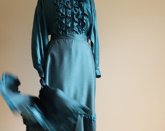 May include: A teal blue satin blouse with a ruffled collar and long sleeves. The blouse is paired with a matching teal blue satin skirt with a ruffled hem.