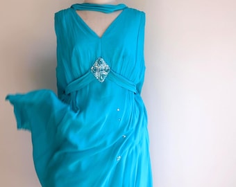 May include: A sleeveless turquoise dress with a V-neckline and a jeweled embellishment at the bust. The dress has a flowing skirt and is displayed on a white mannequin.