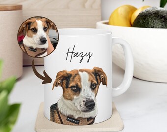 May include: White ceramic mug with a brown and white dog illustration and the name "Hazy" written in black cursive. The mug is on a beige coaster.