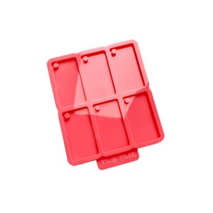 Op de afbeelding: Een koraalkleurige siliconen mal met zes rechthoekige compartimenten, elk met een klein gaatje aan de bovenkant. De mal is ontworpen voor knutselen en heeft de tekst "Meltz Molds" op een klein lipje.