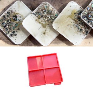 May include: Four square resin coasters with a white base, featuring iridescent shell pieces and gold details. A pink silicone mould with four square sections is also visible.
