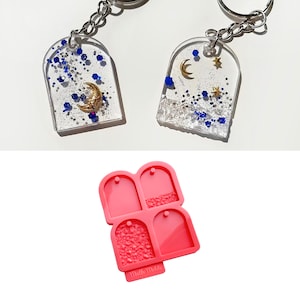 Op de afbeelding: Een set van vier transparante hars sleutelhanger blanco's met een maan- en sterrendesign. De blanco's bevinden zich in een roze siliconen mal met de tekst "Mello Melds" op de bodem.