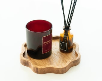 May include: A wooden tray with a scalloped edge holds a red glass candle and a brown glass bottle with black diffuser sticks. The candle label reads "Gingerbread" and the bottle label reads "Aromatherapy".