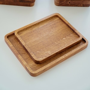 May include: Two wooden serving trays, one stacked on top of the other. The trays are made of light brown wood and have a rectangular shape. The trays are ideal for serving snacks, appetisers, or desserts.