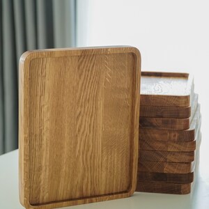 May include: A set of wooden serving trays, one large tray and a stack of smaller trays. The trays are made of light brown wood with a natural finish.
