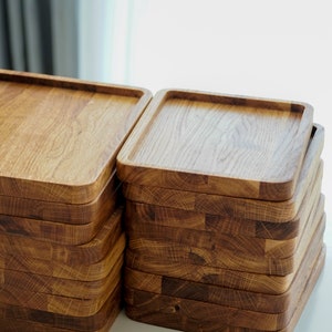 May include: Two stacks of wooden serving trays, each stack is made of multiple square trays, the trays are a light brown color and have a natural wood grain.