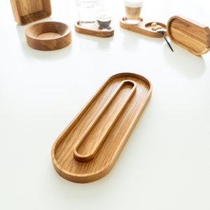 Op de afbeelding: Houten serveerplanken en onderzetters in diverse vormen. De planken omvatten een lang ovale plank met een kleinere ovale inzet, een vierkante plank en ronde onderzetters. De onderzetters bevatten glazen water en koffie.