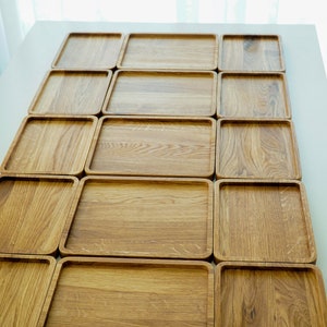 May include: A set of 15 wooden serving trays arranged in a grid pattern. The trays are made of light brown wood and have a smooth, polished finish.