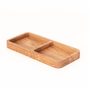 Puede incluir: Una bandeja de madera con dos compartimentos. La bandeja es de madera marrón claro y tiene forma rectangular.