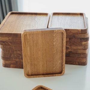 May include: A stack of wooden serving trays with a natural wood finish. The trays are square and have a raised edge.