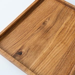 May include: A rectangular wooden serving tray with a raised edge. The tray is made of light brown wood with visible grain patterns and a knot. The tray is likely used for serving food or displaying items.