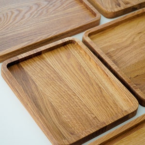 Puede incluir: Una colección de bandejas rectangulares de madera con esquinas redondeadas. Las bandejas son de madera marrón claro, mostrando un patrón de vetas natural. Las bandejas están dispuestas sobre una superficie blanca.