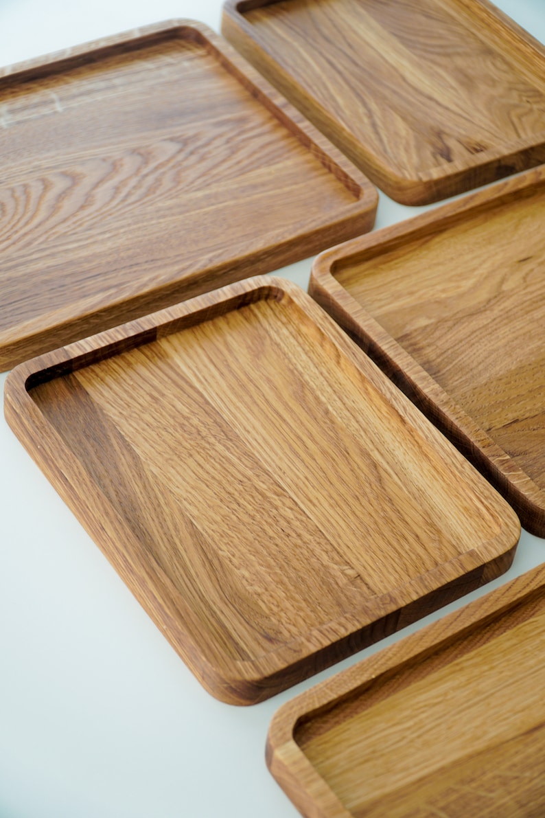 May include: Four wooden serving trays of varying sizes, all made of light brown wood with a natural grain pattern. The trays are arranged in a staggered pattern, with the largest tray at the top and the smallest tray at the bottom.