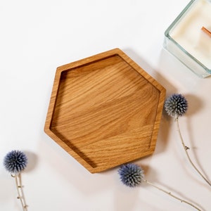 Könnte beinhalten: Ein sechseckiges Holztablett mit einer natürlichen Holzoptik. Das Tablett befindet sich auf einer weißen Oberfläche mit zwei blauen Distelblumen.