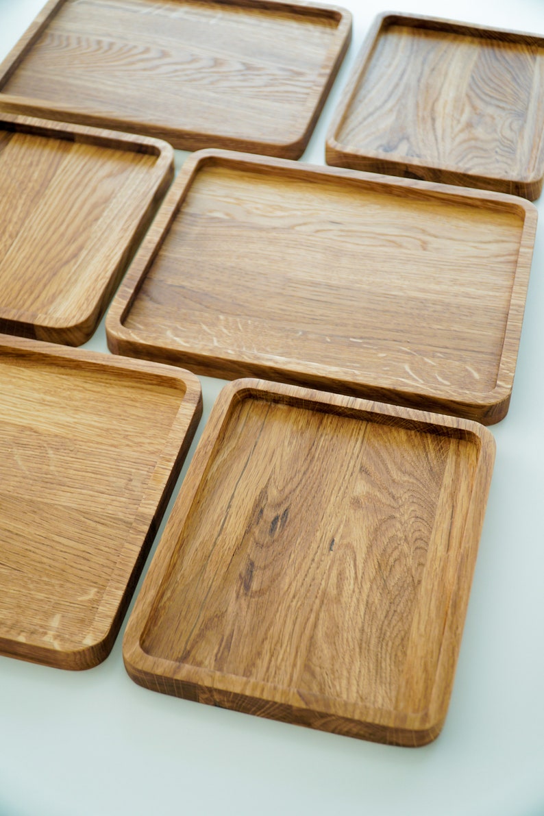 May include: Five wooden serving trays of varying sizes, arranged in a staggered pattern on a white surface. The trays are made of light brown wood with a natural grain pattern.