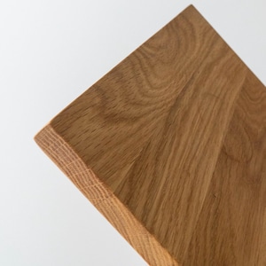 Puede incluir: Primer plano de una tabla de cortar de madera con veta natural. La tabla es cuadrada con un borde biselado. La madera es de color marr&oacute;n claro y tiene una textura suave. El fondo es blanco.