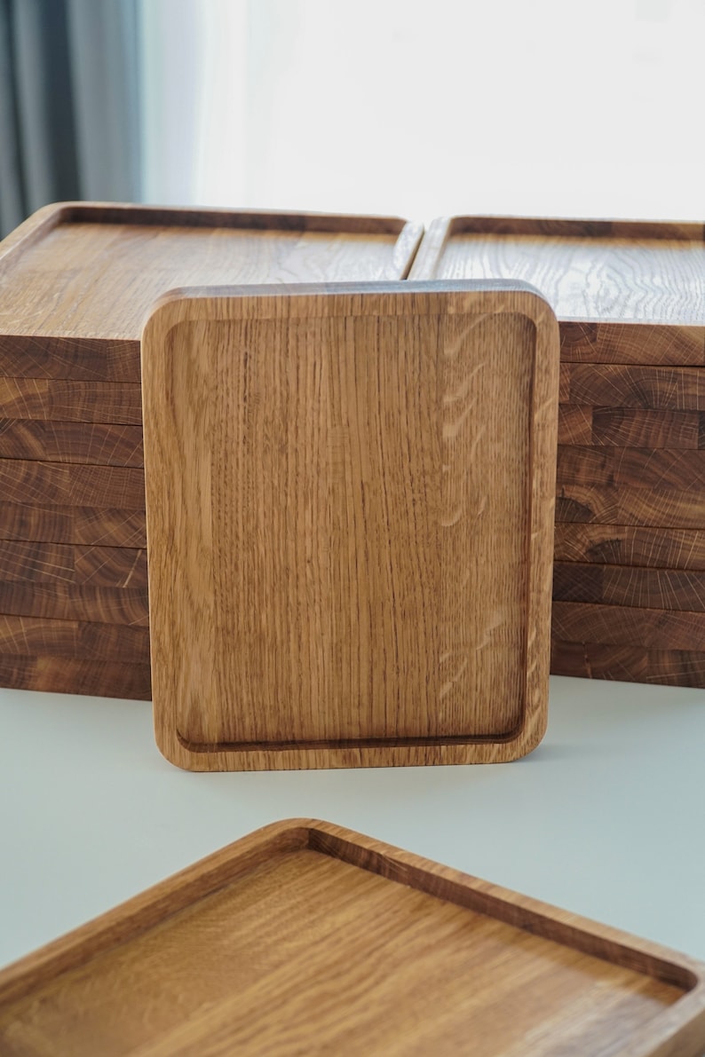 May include: A stack of square wooden serving trays with a natural wood finish. The trays are made of solid wood and have a smooth surface.