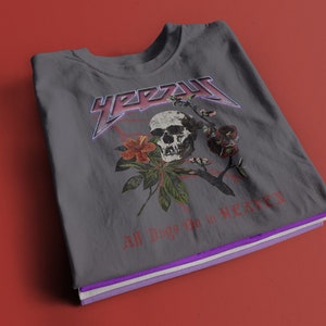 May include: Gray t-shirt with a skull and floral design. The text "YEEZY" is printed in a metallic font above the skull. The text "All Things Go to Heaven" is printed below the skull.