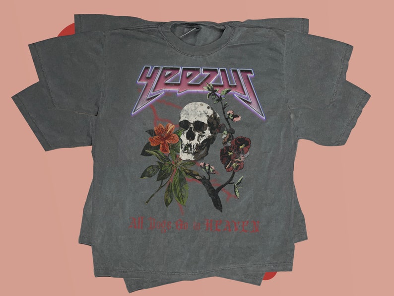 May include: A gray t-shirt with a skull and flowers graphic. The text "YEEZY" is printed in a large, bold font above the graphic. The text "All Love is Heavy" is printed below the graphic.