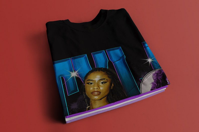 May include: Black t-shirt with a graphic print of a woman's face with blue and purple accents. The text "MILK" is printed in large blue letters.