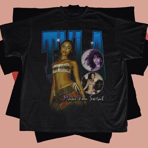 May include: Black t-shirt with a vintage-style graphic featuring a woman with the text "Tila Make You Sweat".