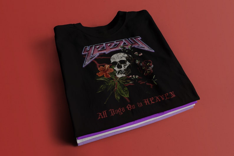 May include: Black t-shirt with a skull and floral design. The text "YEEZY" is printed in a large, bold font above the skull. The text "All Dogs Go to HEAVEN" is printed below the skull.