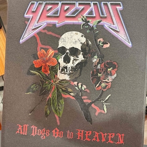 May include: A dark gray t-shirt with a skull and floral design. The skull is white with black details and is surrounded by red and white flowers. The text "Y2ZZU" is in pink and purple with a lightning bolt design. The text "All Dogs Go to HEAVEN" is in red.