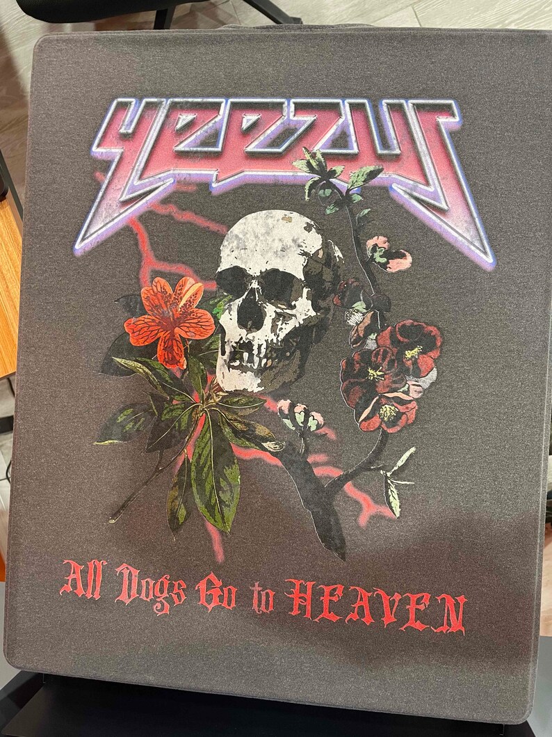 May include: A dark gray t-shirt with a skull and floral design. The skull is white with black details and is surrounded by red and white flowers. The text "Y2ZZU" is in pink and purple with a lightning bolt design. The text "All Dogs Go to HEAVEN" is in red.
