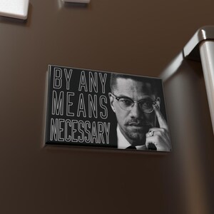 Könnte beinhalten: Ein rechteckiger Schwarz-Weiß-Magnet mit dem Text "BY ANY MEANS NECESSARY" und einem Porträt eines Mannes mit Brille. Der Magnet ist an einer dunkelbraunen Kühlschranktür mit weißen quadratischen Magneten befestigt.
