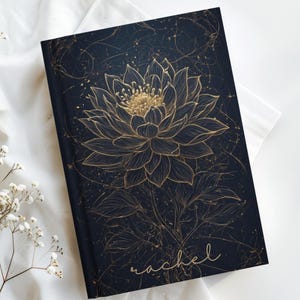 May include: A dark navy blue hardcover journal featuring a gold line-art illustration of a large blooming flower with intricate petals and stems. The name Rachel is written in a gold cursive script at the bottom right corner of the front cover.