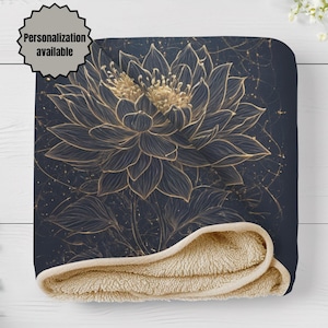 Op de afbeelding: Een donker marineblauwe deken met een groot, gedetailleerd goudkleurig lijntekeningontwerp van een lotusbloem en een zachte, beige sherpa-fleece voering. Een ronde badge in de linkerbovenhoek bevat de tekst Personalization available.