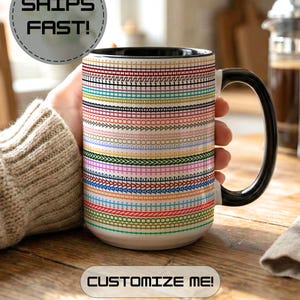May include: A ceramic mug with a black interior and handle, featuring a white exterior decorated with numerous horizontal rows of colourful, varied embroidery-style stitch patterns. The mug includes the text SHIPS FAST! and CUSTOMIZE ME!