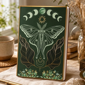 Peut inclure: Un carnet à couverture rigide vert foncé orné d'une illustration centrale de papillon de nuit, d'un symbole solaire et d'un cycle lunaire. La couverture présente des contours de feuilles dorés et du feuillage vert, bordée d'un liseré doré.